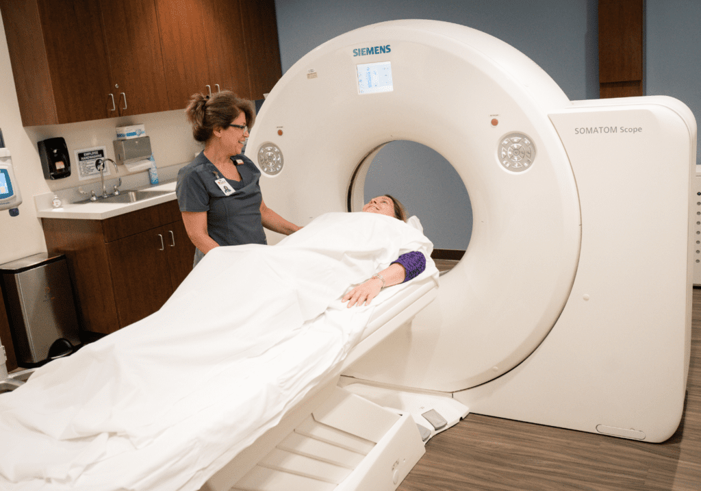 Radiology technician standing over patient in gown laying on exam table getting an CT at iCare Emergency Room and Urgent Care