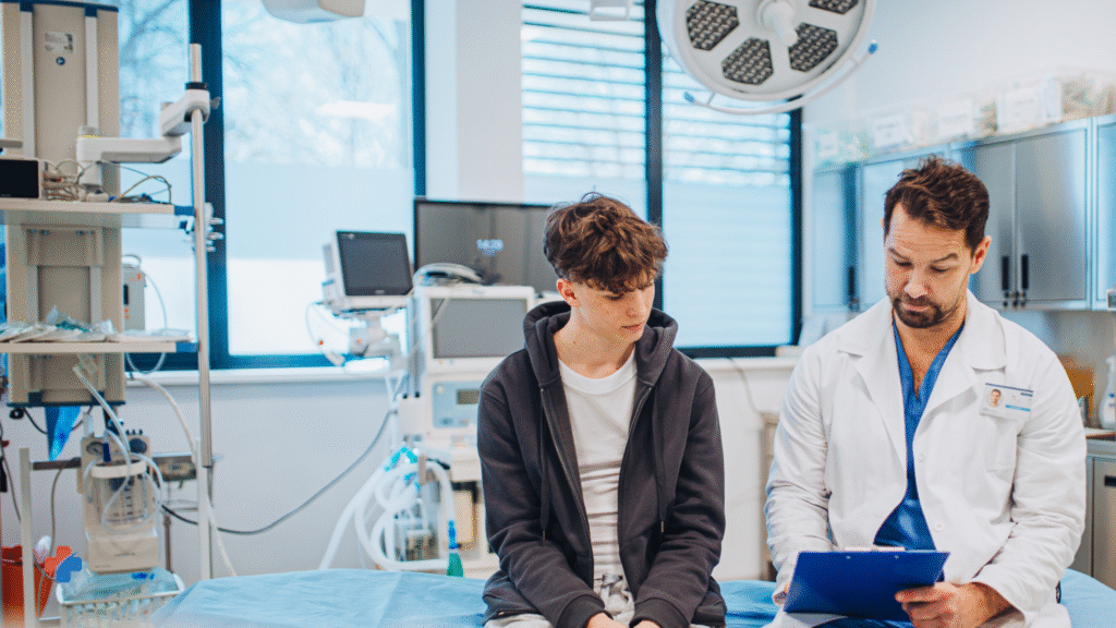 doctor holding clip board talking to a teenager while both are sitting side by side in a medical office. depicting a doctor going over test results for covid test, mono test, flu test etc.