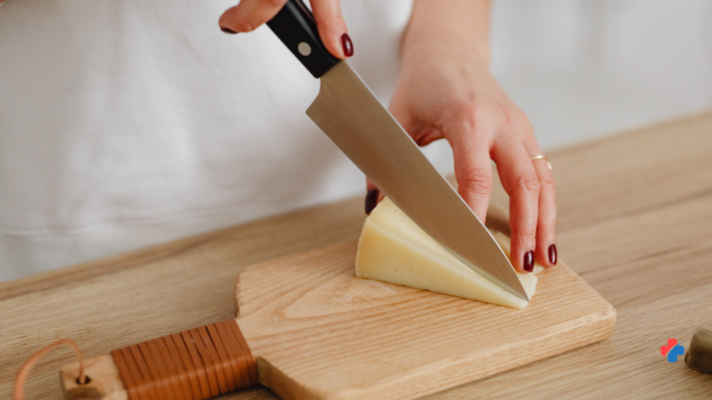 a woman's hand cutting a block of cheese. demonstrating safe cutting skills to prevent knife cuts and kitchen injuries